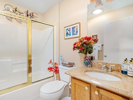 full bathroom with a textured ceiling, bath / shower combo with glass door, toilet, and vanity