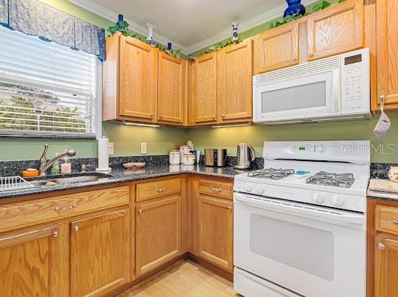 kitchen with sink, dark stone countertops, white appliances, and ornamental molding