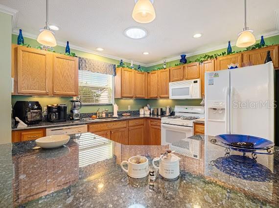 kitchen featuring pendant lighting, white appliances, crown molding, and dark stone counters