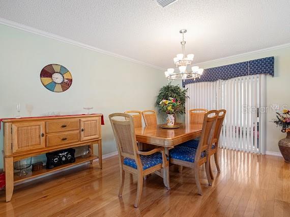 dining space featuring light wood-type flooring, ornamental molding, a notable chandelier, and a textured ceiling