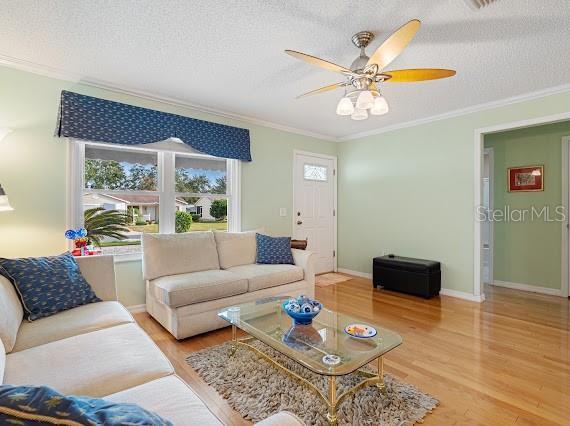 living room with light wood-type flooring, ceiling fan, crown molding, and a textured ceiling