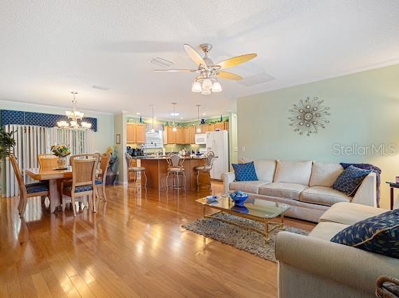 living room with ornamental molding, ceiling fan with notable chandelier, light hardwood / wood-style flooring, and a textured ceiling