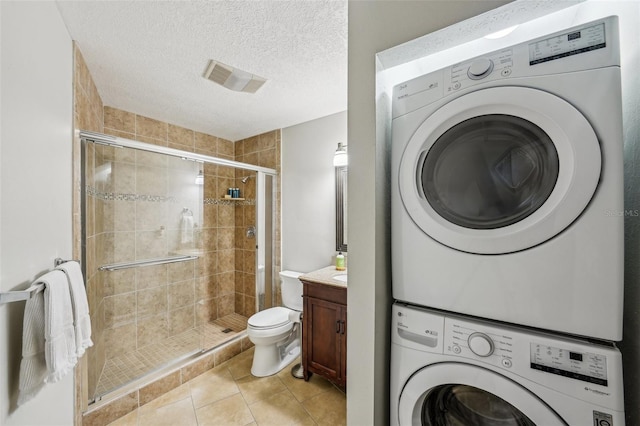 bathroom featuring stacked washer and dryer, tile patterned floors, walk in shower, a textured ceiling, and vanity