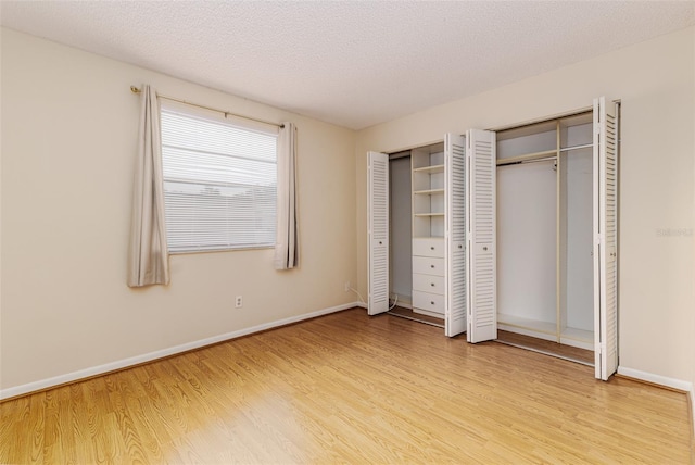 unfurnished bedroom featuring two closets, a textured ceiling, and light hardwood / wood-style flooring