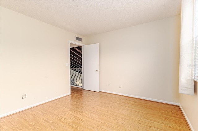 empty room with a textured ceiling and light hardwood / wood-style floors