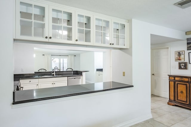 kitchen with kitchen peninsula, white cabinets, stainless steel dishwasher, light tile patterned flooring, and sink