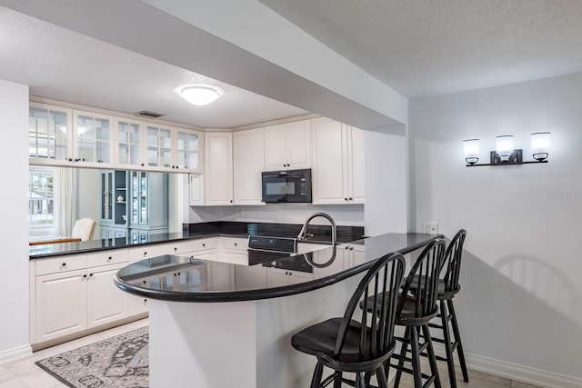 kitchen featuring electric range oven, sink, white cabinets, kitchen peninsula, and a breakfast bar area