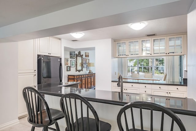 kitchen with black refrigerator, white cabinetry, light tile patterned floors, and kitchen peninsula