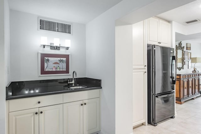 kitchen with black fridge, white cabinetry, light tile patterned floors, and sink