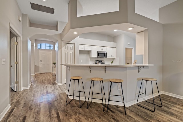 kitchen with a high ceiling, stainless steel appliances, white cabinetry, and a kitchen breakfast bar