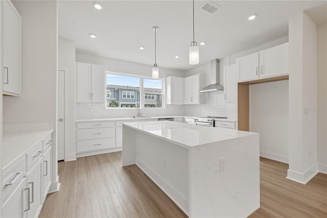 kitchen with sink, white cabinetry, a center island, stainless steel range with electric stovetop, and wall chimney range hood