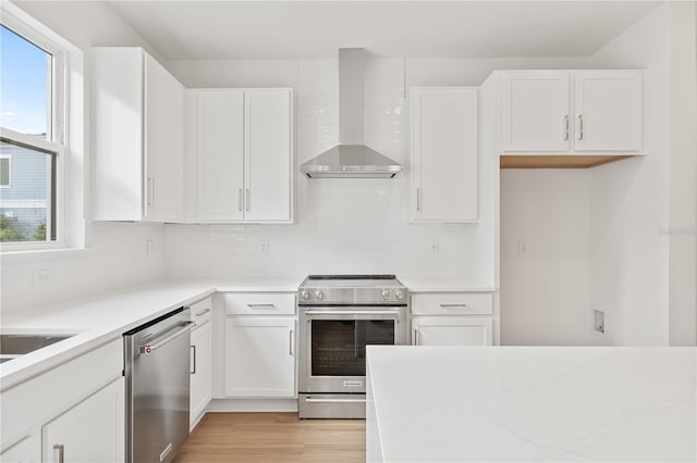 kitchen featuring white cabinets, wall chimney exhaust hood, light wood-type flooring, decorative backsplash, and appliances with stainless steel finishes