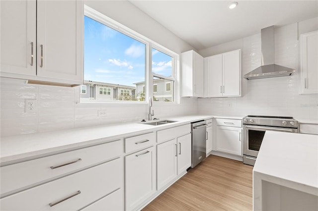 kitchen with stainless steel appliances, sink, white cabinets, wall chimney exhaust hood, and light hardwood / wood-style floors