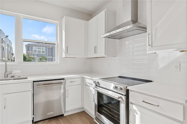 kitchen with stainless steel appliances, wall chimney range hood, sink, and white cabinetry