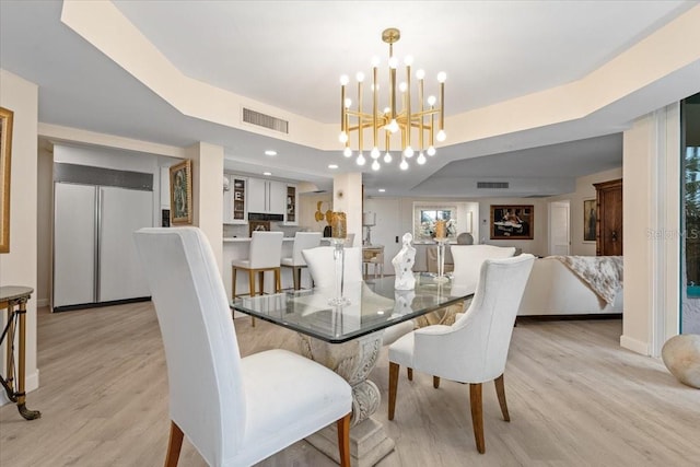 dining space featuring a chandelier, a raised ceiling, and light hardwood / wood-style flooring