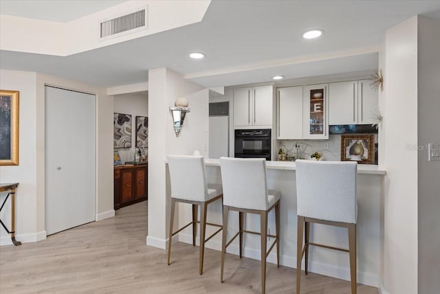 kitchen with a breakfast bar area, light hardwood / wood-style flooring, kitchen peninsula, oven, and backsplash