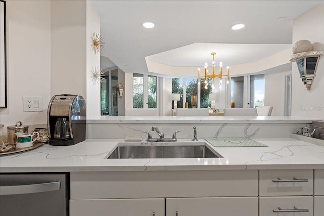 kitchen with sink, dishwasher, white cabinetry, light stone counters, and a chandelier