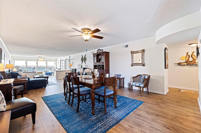 dining room with ceiling fan, a textured ceiling, crown molding, and light wood-type flooring