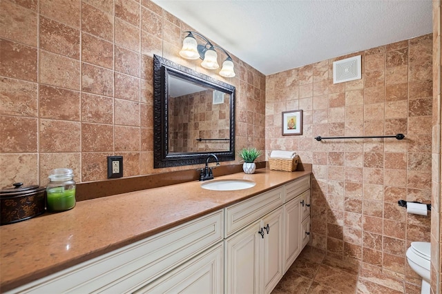 bathroom featuring toilet, a textured ceiling, tile walls, and vanity