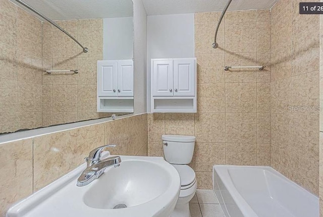 full bathroom with toilet, a textured ceiling, tile walls, tiled shower / bath, and sink