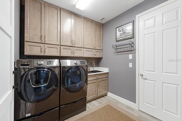 clothes washing area featuring sink, a textured ceiling, cabinets, separate washer and dryer, and light hardwood / wood-style flooring