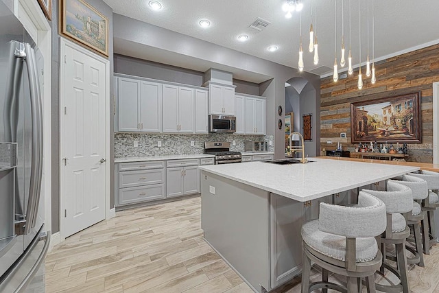 kitchen featuring hanging light fixtures, stainless steel appliances, a center island with sink, backsplash, and sink