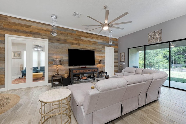 living room featuring ceiling fan, french doors, and wooden walls