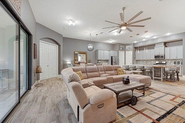 living room featuring ceiling fan with notable chandelier, light wood-type flooring, and a textured ceiling