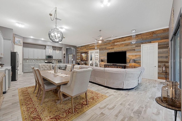 dining area featuring ceiling fan, light hardwood / wood-style flooring, wooden walls, and a textured ceiling