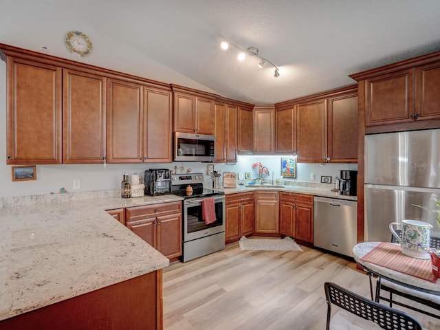 kitchen with stainless steel appliances, sink, vaulted ceiling, light stone counters, and light hardwood / wood-style flooring