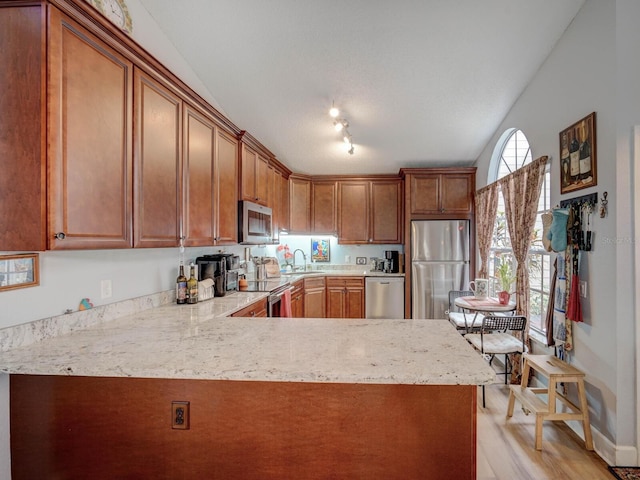 kitchen with kitchen peninsula, light wood-type flooring, track lighting, stainless steel appliances, and light stone counters