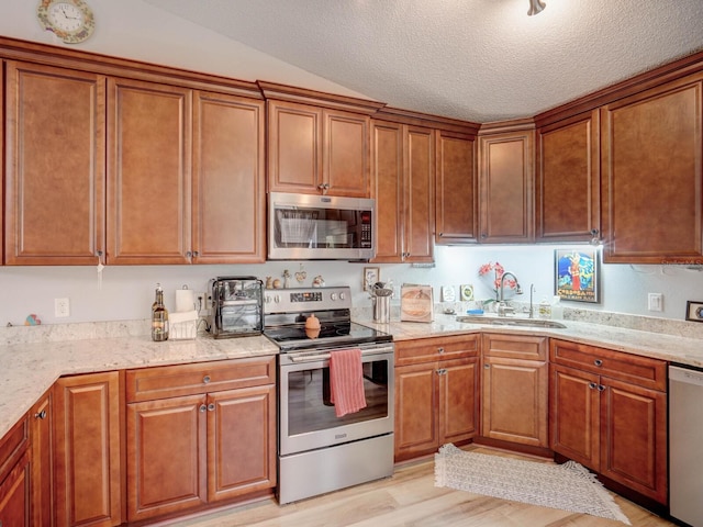 kitchen with lofted ceiling, sink, light wood-type flooring, appliances with stainless steel finishes, and light stone counters