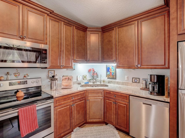 kitchen with appliances with stainless steel finishes, sink, light stone counters, and a textured ceiling