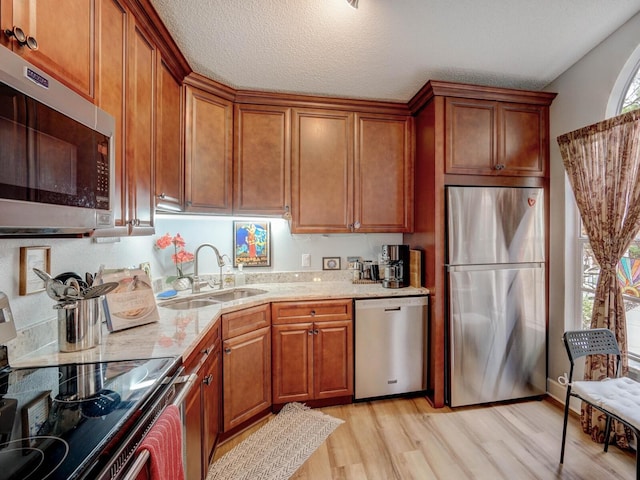 kitchen featuring a textured ceiling, stainless steel appliances, sink, light stone counters, and light hardwood / wood-style flooring