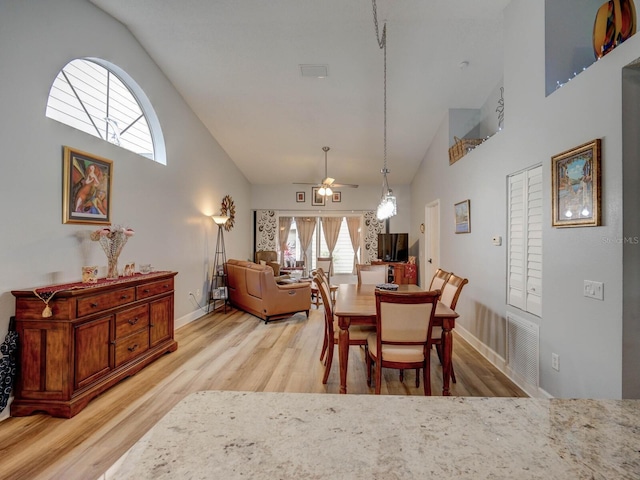 dining room with ceiling fan, light hardwood / wood-style floors, and high vaulted ceiling