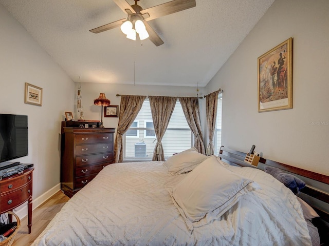 bedroom with ceiling fan, light hardwood / wood-style floors, a textured ceiling, and lofted ceiling