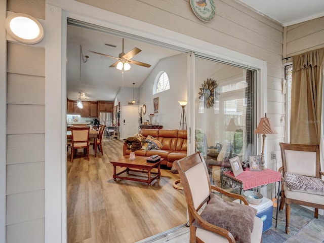 living area with lofted ceiling, ceiling fan, wooden walls, and light hardwood / wood-style floors