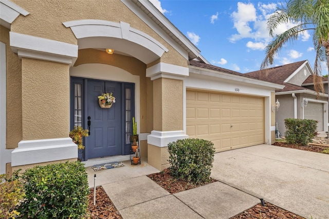 property entrance with a garage, driveway, and stucco siding