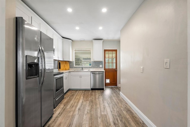 kitchen with stainless steel appliances, tasteful backsplash, white cabinets, wood-type flooring, and sink