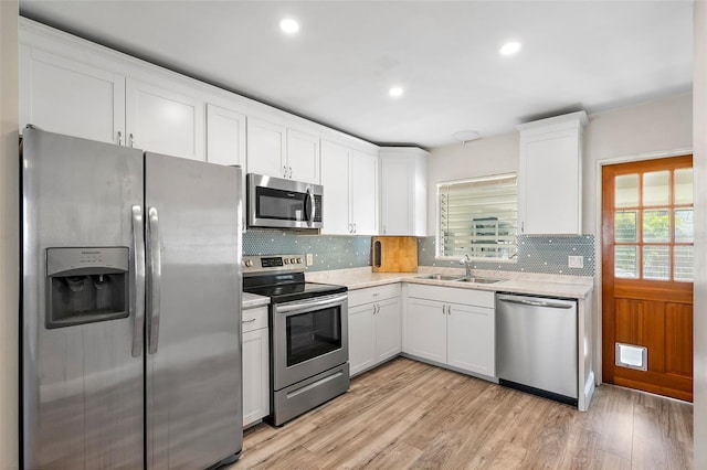 kitchen featuring light wood-type flooring, appliances with stainless steel finishes, white cabinetry, and sink