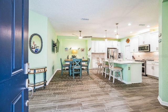 kitchen with ceiling fan, decorative backsplash, hanging light fixtures, a kitchen island with sink, and stainless steel appliances