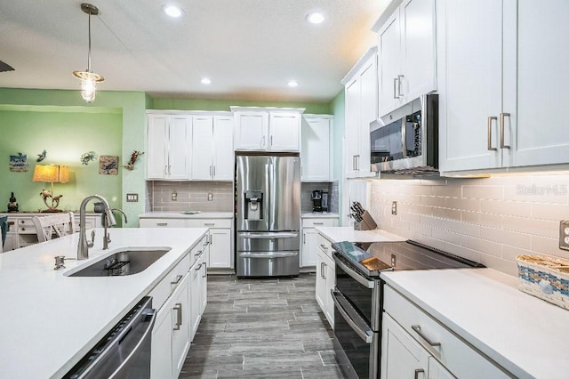 kitchen with stainless steel appliances, pendant lighting, white cabinetry, and sink