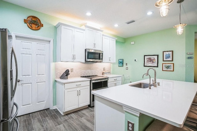 kitchen with white cabinets, appliances with stainless steel finishes, decorative light fixtures, sink, and a kitchen island with sink