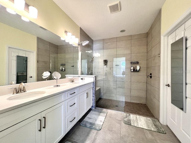 bathroom with a textured ceiling, vanity, a tile shower, and tile patterned flooring