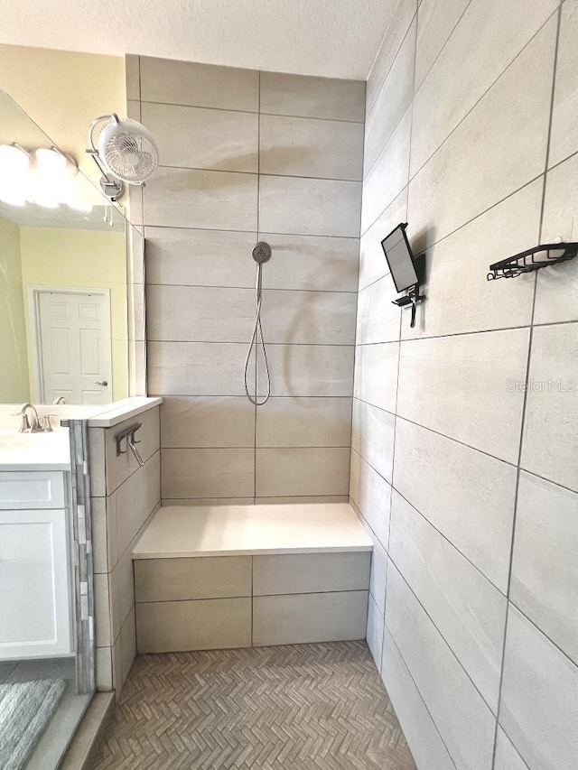 bathroom featuring a textured ceiling, a tile shower, and vanity