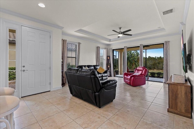 tiled living room featuring a raised ceiling, ceiling fan, and crown molding