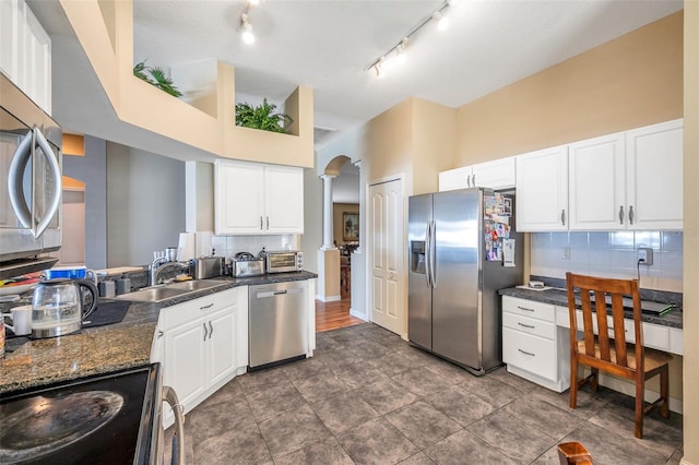 kitchen featuring backsplash, sink, white cabinetry, stainless steel appliances, and dark stone counters