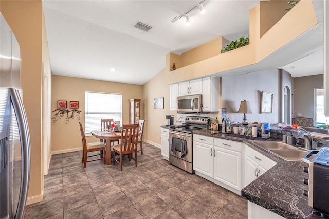 kitchen featuring rail lighting, stainless steel appliances, vaulted ceiling, white cabinets, and sink