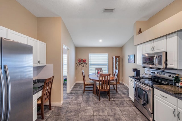 kitchen with vaulted ceiling, stainless steel appliances, dark stone countertops, and white cabinets