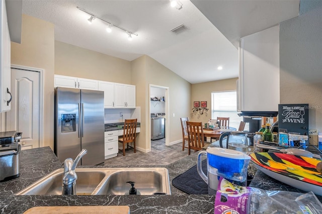 kitchen featuring stainless steel refrigerator with ice dispenser, vaulted ceiling, white cabinets, washer / clothes dryer, and sink